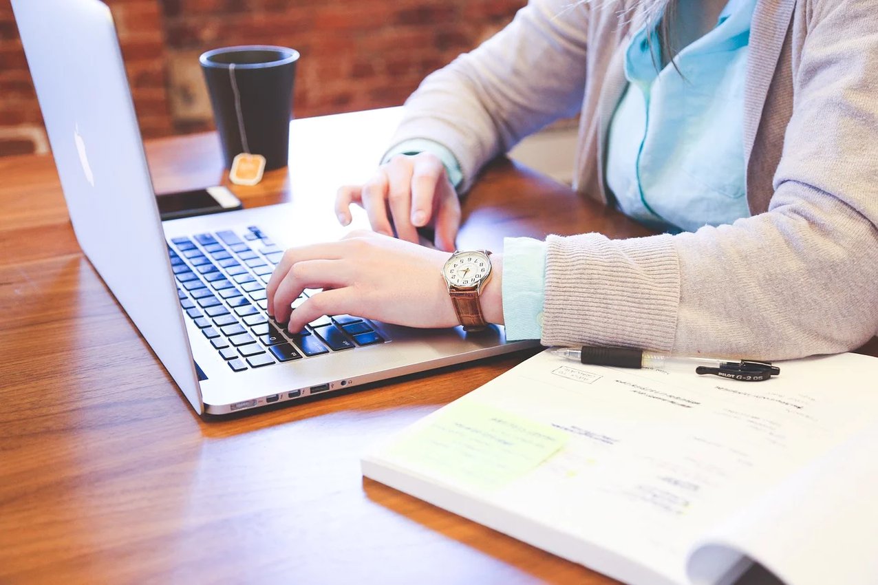 Persona che lavora su una scrivania con un laptop, un quaderno e una tazza di caffè